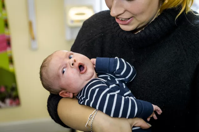 Bebis som gäspar i sin mammas famn. Foto.