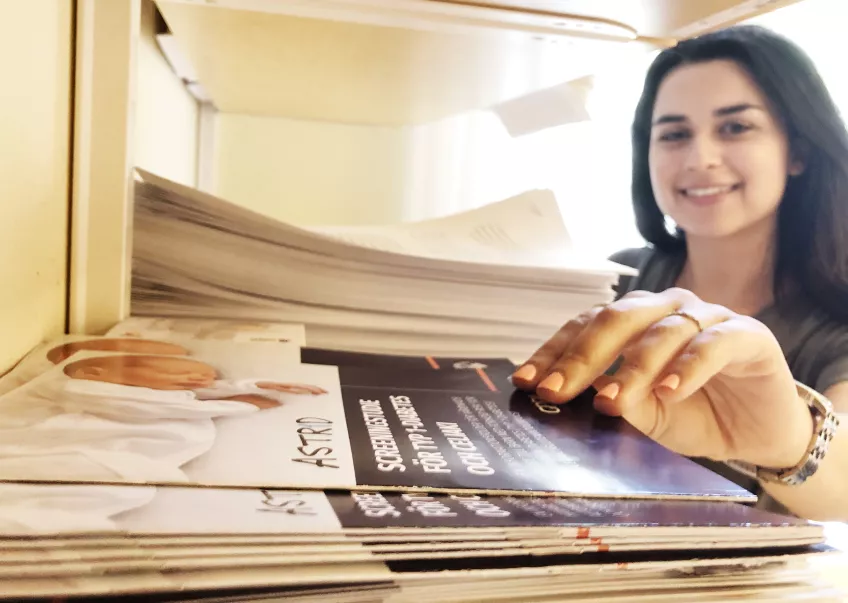 Sara Maraoufkhani sträcker sig efter information om Astridstudien i en bokhylla. Foto.